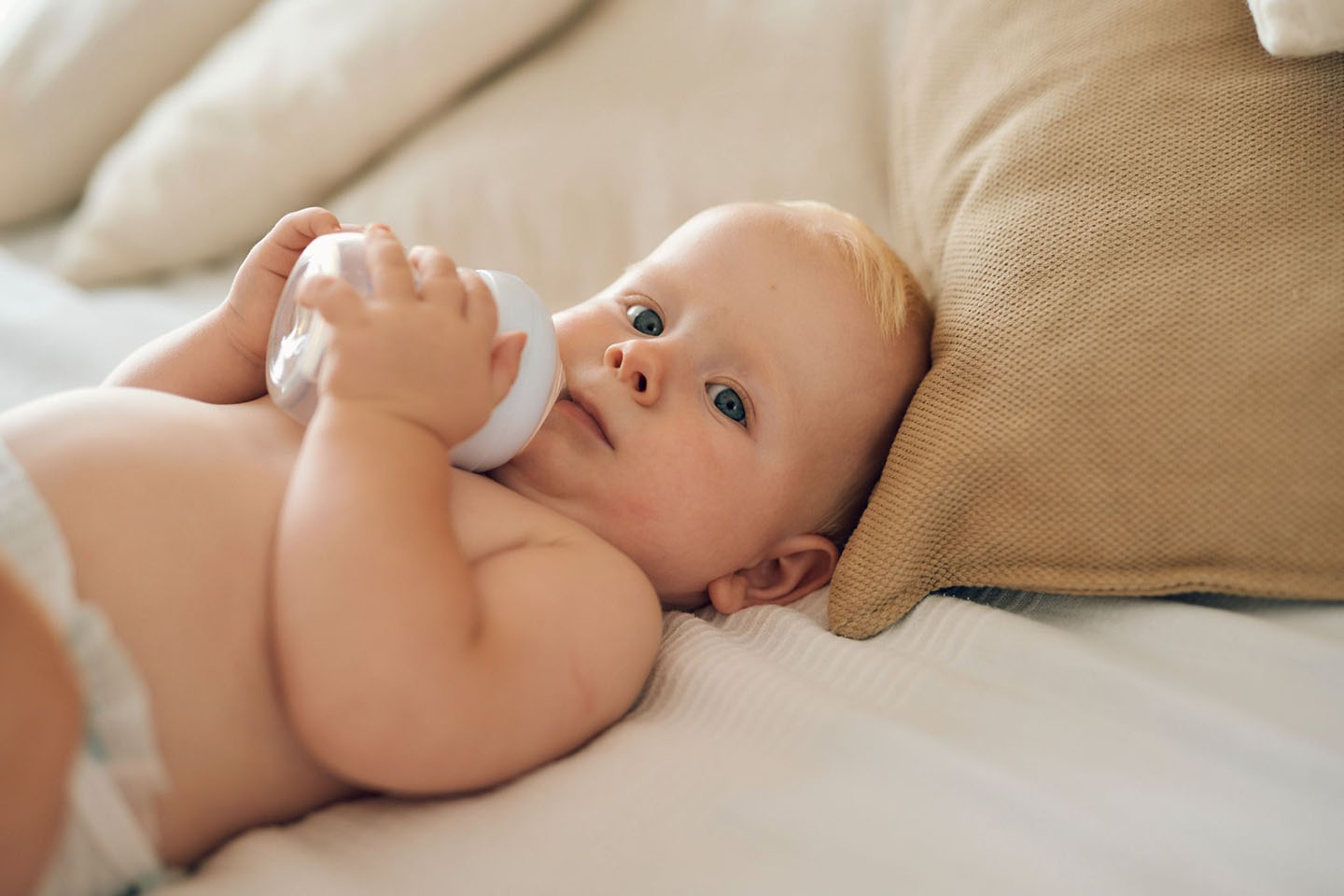 Бебе лежи на легло и пие мляко от шише