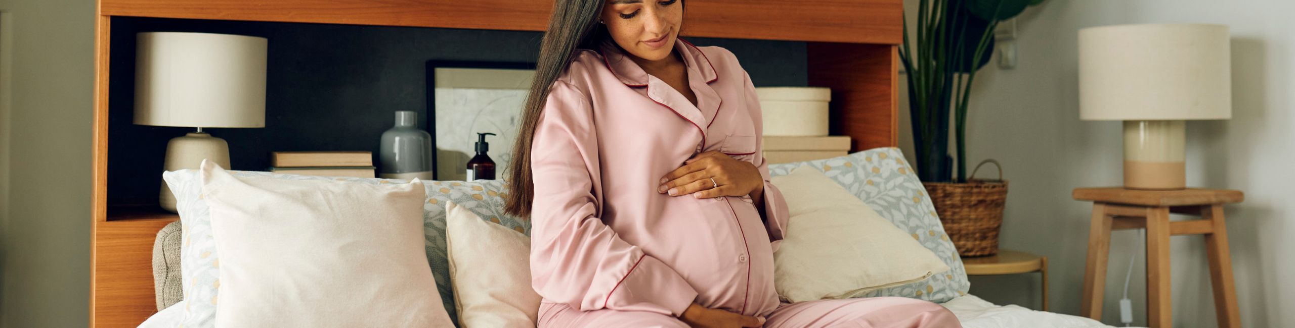 Бременна жена, седнала в леглото и докосваща корема си - значението на витамините по време на бременност
