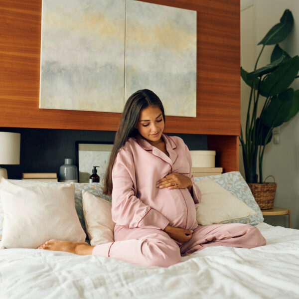 Бременна жена, седнала в леглото и докосваща корема си - значението на витамините по време на бременност