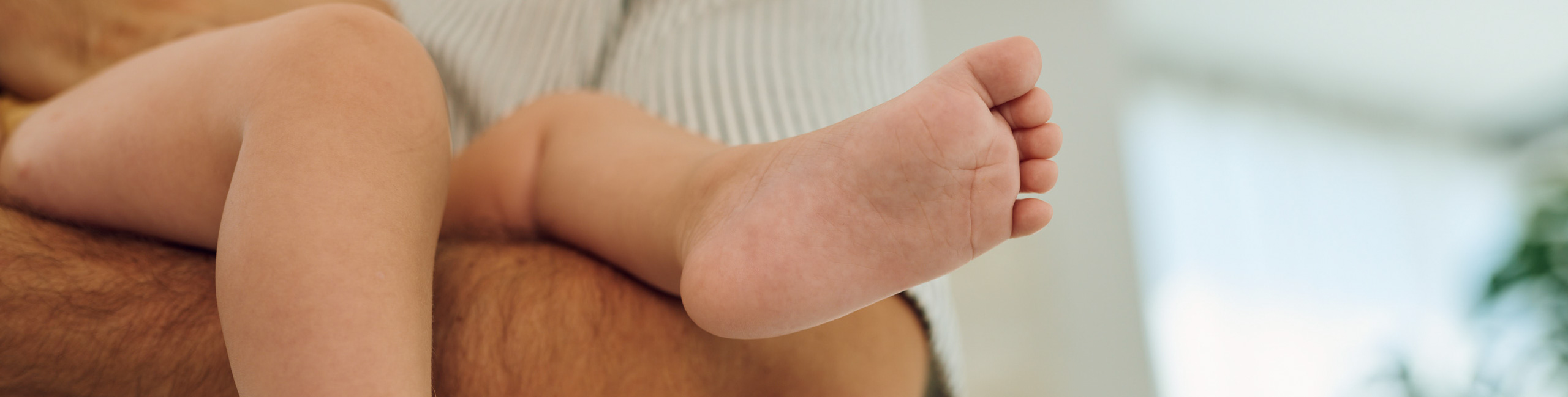 Краката на бебето в ръцете на родителите.