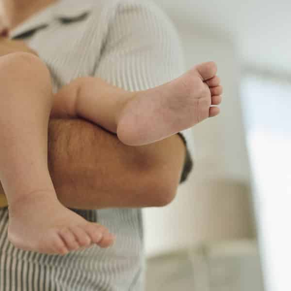 Краката на бебето в ръцете на родителите.