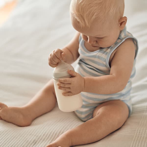 Бебето седи на леглото с шише мляко Новалак.