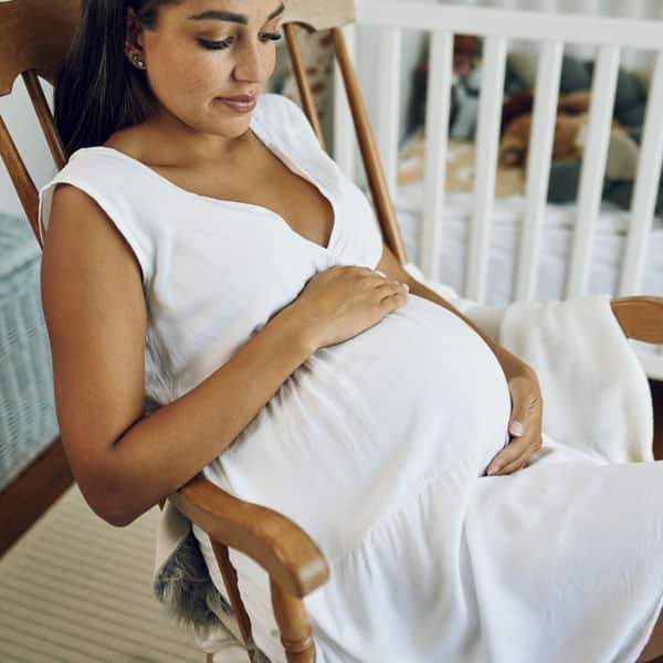 Бременна жена седи на стол и гали корема си.