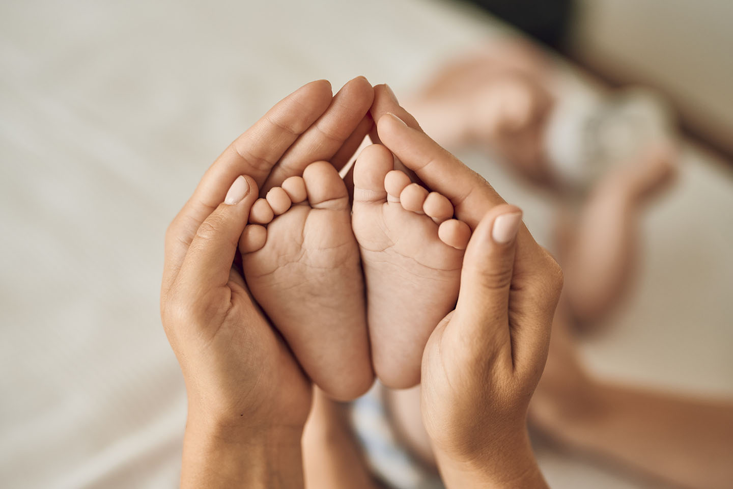 Краката на бебето в ръцете на майката