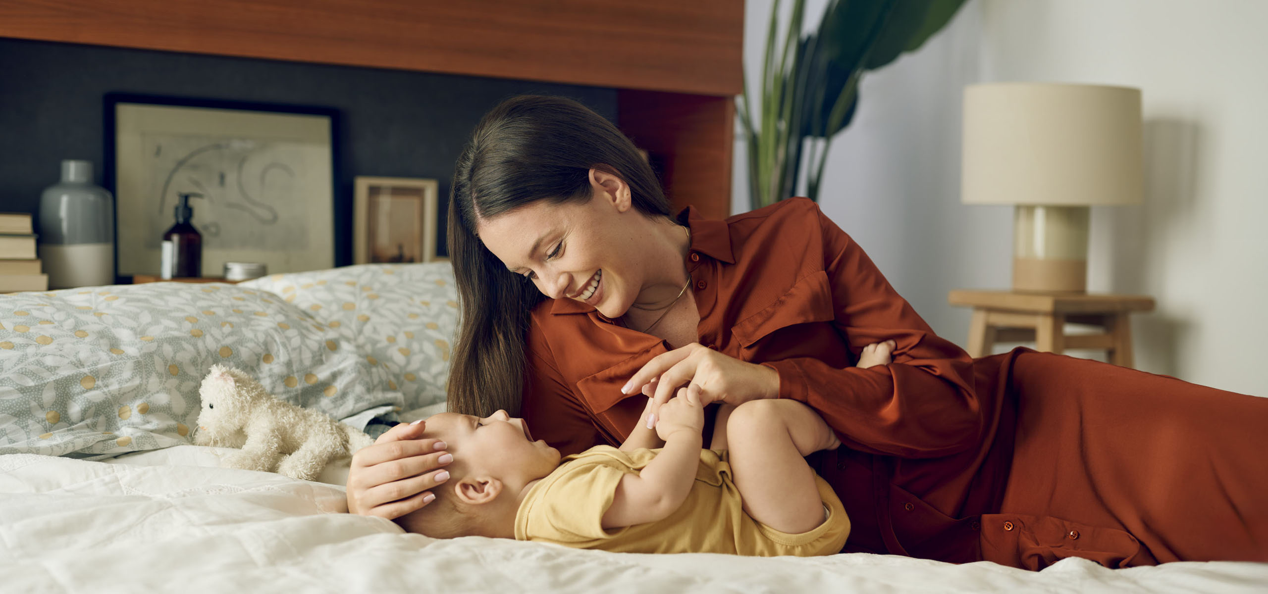 Мама си играе с бебето на леглото.