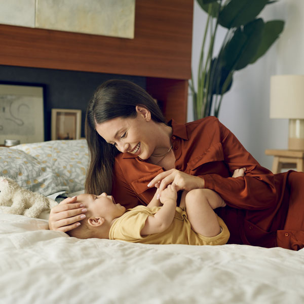 Мама си играе с новородено бебе в леглото