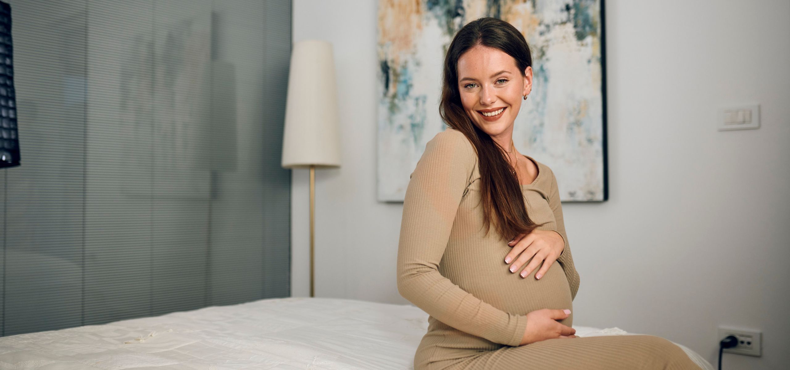 Бременна жена седи на леглото и гали корема си