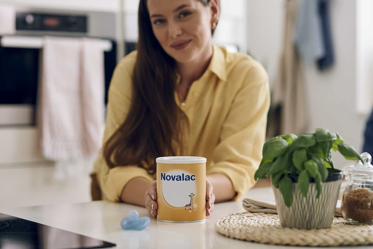 Усмихната майка, държаща кутия с адаптирано мляко за кърмачета Novalac