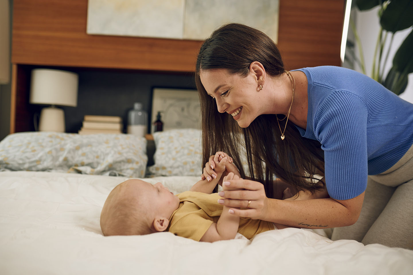 Майка си играе с бебето на леглото.