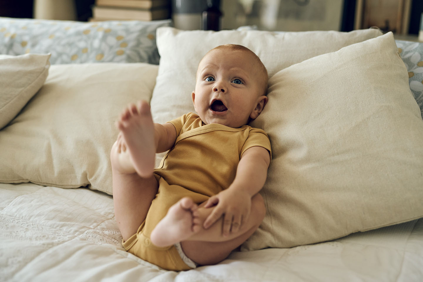 Бебето лежи щастливо на възглавниците и повдига крачетата си.