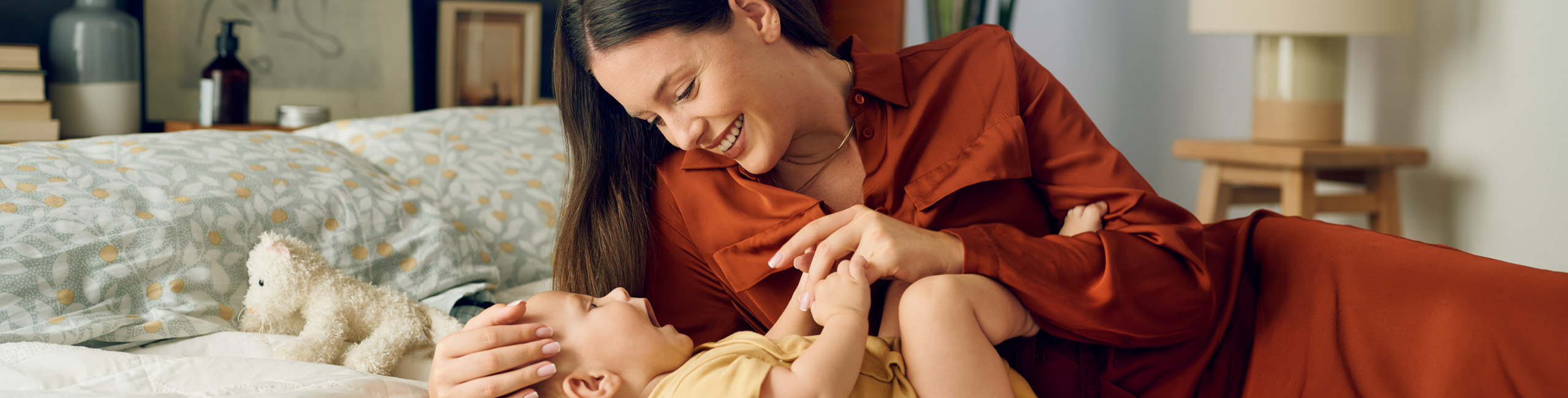 Майка си играе с бебето на леглото.